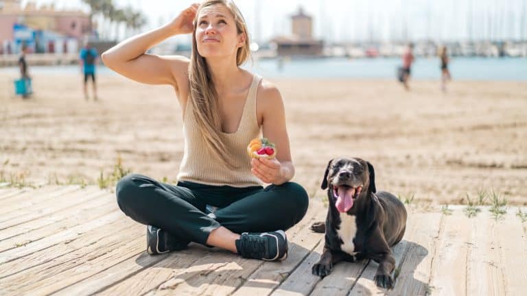 Young blonde woman with her dog holding a tartlet at outdoors having doubts and with confuse face expression