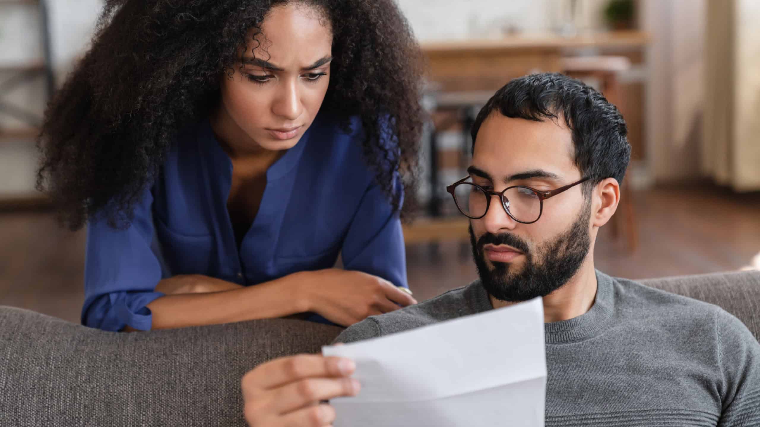 Budget Planning. Stressed thoughtful mixed race couple african arabian spouses holding papers and calculating family spends together checking documents, suffering financial crisis, closeup shot