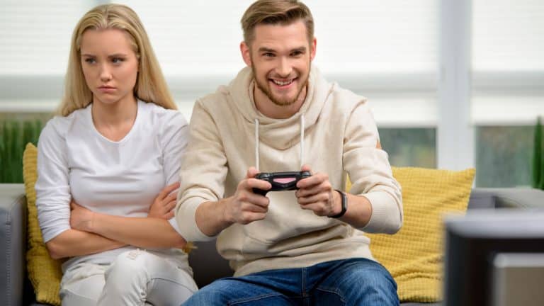 Video games concept. Young annoyed girlfriend waiting for her boyfriend to stop playing video games. Nice apartment interior
