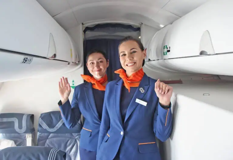 Flight attendants on a plane waving at the camera and smiling