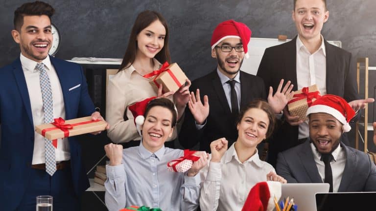 Happy business team enjoying Christmas party in office, holding gift boxes after Secret Santa game, smiling at camera