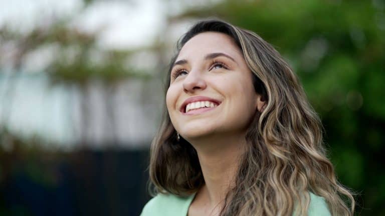 Portrait of a grateful contemplative young woman closeup face. Meditative 20s girl opening eyes to sky with gratitude