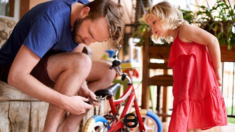 Bicycle, repair and man in home with kid for help, teaching and learning together for bonding with daughter. Maintenance, support and dad fixing bike for girl with tools, care and child development