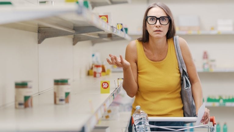 Desperate young woman doing grocery shopping during a recession, the supermarket shelves are almost empty, supply shortage concept