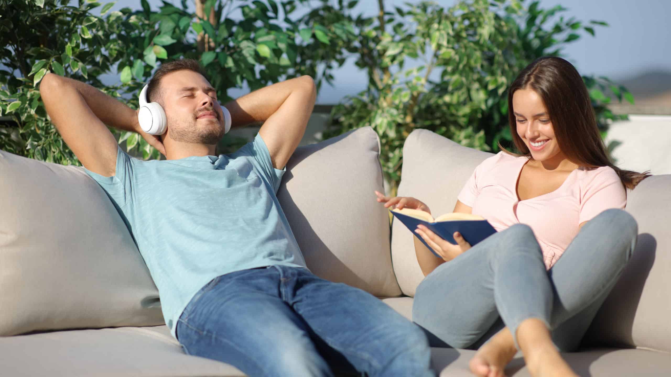 Happy couple spending time with different hobbies sitting in a sofa in a terrace at hoke a sunny day