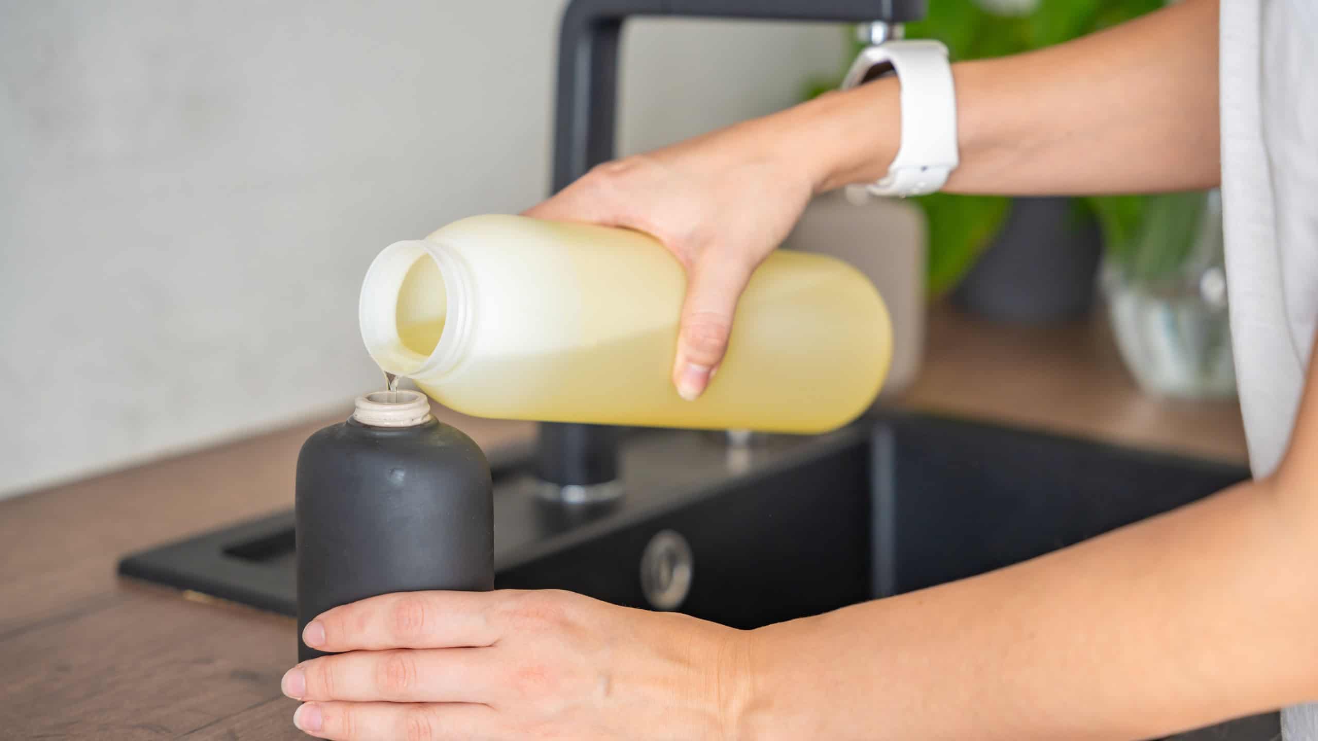 A woman pours soap or detergent from recycled packaging into a reusable bottle in kitchen. Eco-friendly lifestyle concept. High quality photo