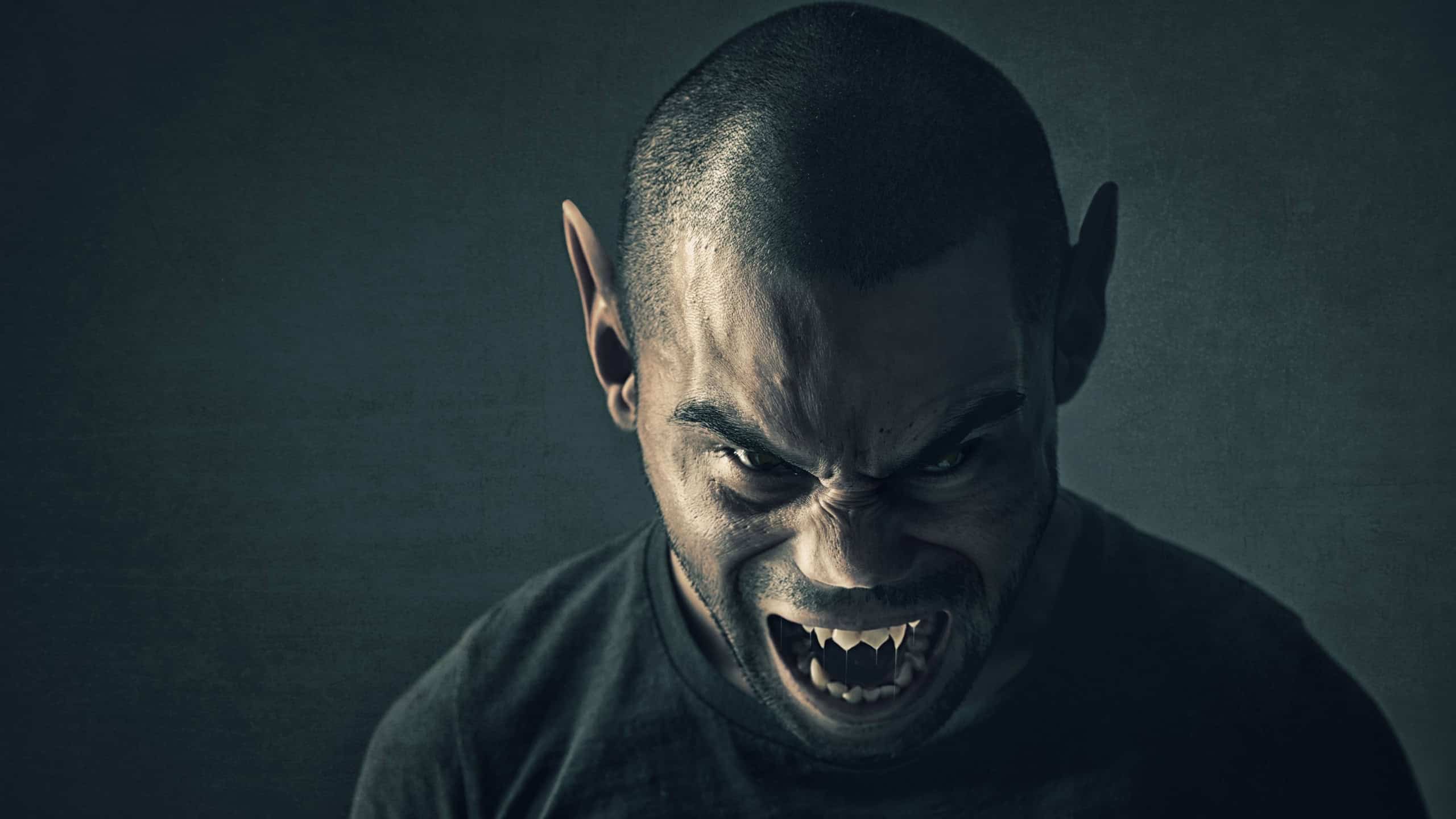 Monster, man and face with horror in studio for fantasy, demon and angry vampire with fangs, scary and terror. Werewolf, devil and creepy creature with shouting, rage and surreal on black background