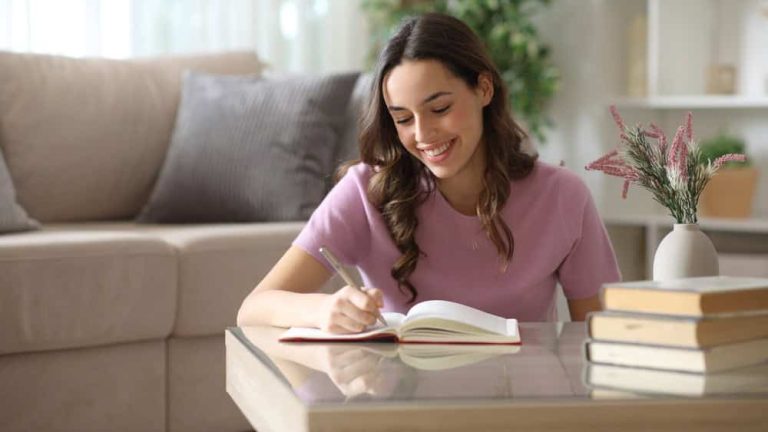 Happy woman writing in paper agenda over coffee table at home