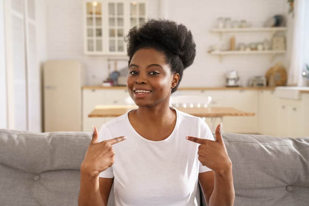 Black girl talking in webinar, points fingers at herself, looking at webcam. Smiling young African woman vlogger influencer make video conference call, looking at camera, recording vlog at home.
