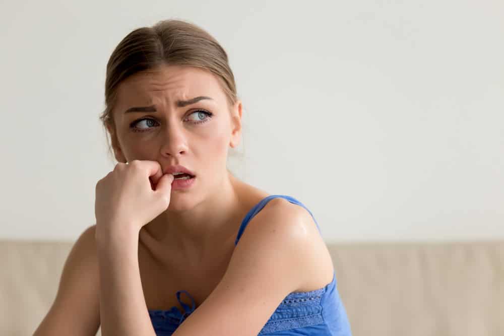 Headshot portrait of worried young woman biting nails and looking aside with fear. Frightened lady thinking about problems, afraid of difficulties, nervous because of bad relationship with boyfriend